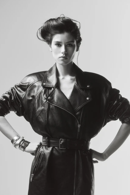 Monochromatic portrait of a woman wearing a black leather jacket and silver bracelets, striking a confident pose against a grey background.