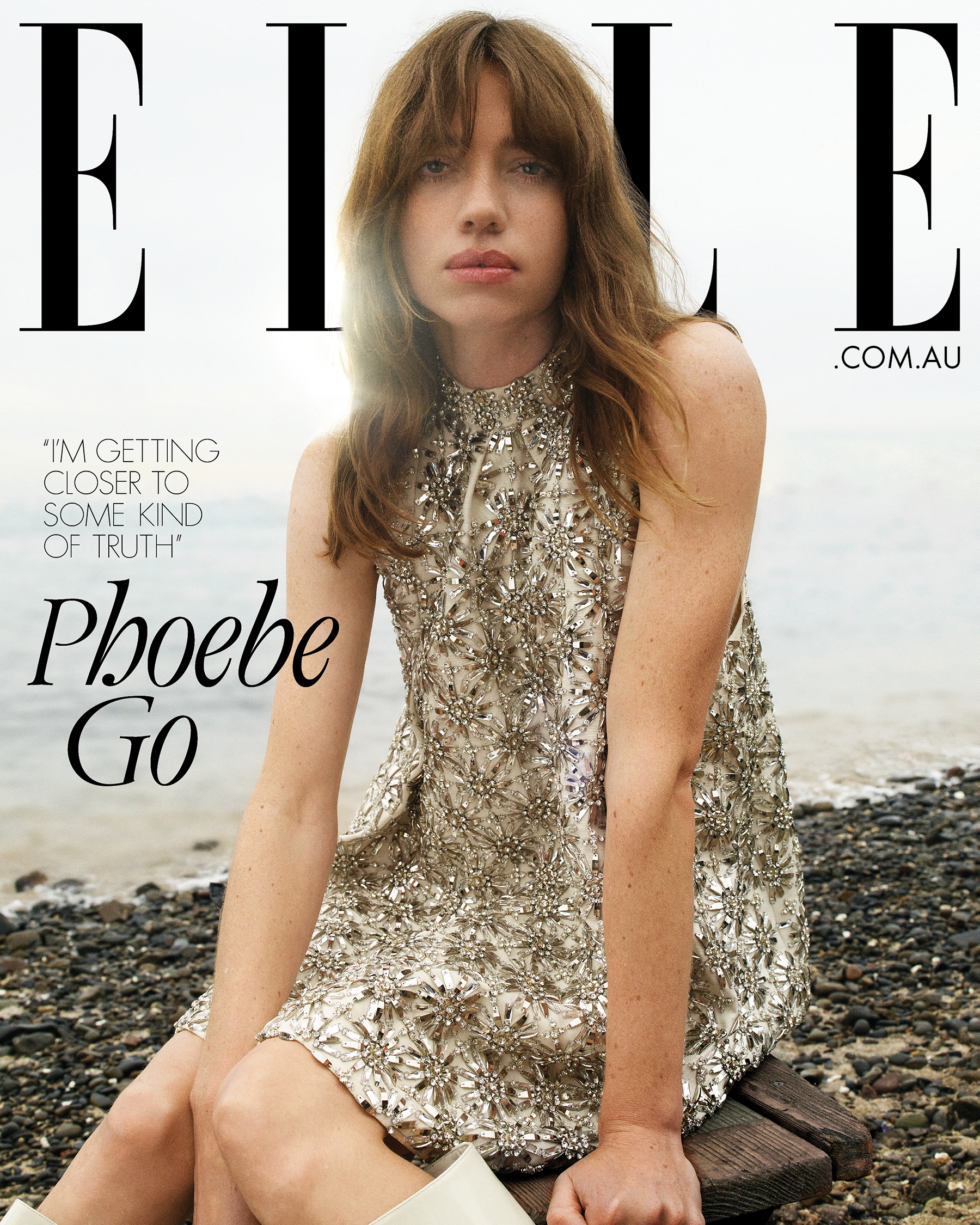 Woman in an embellished silver dress seated on a wooden pier by the water with magazine cover text overlay