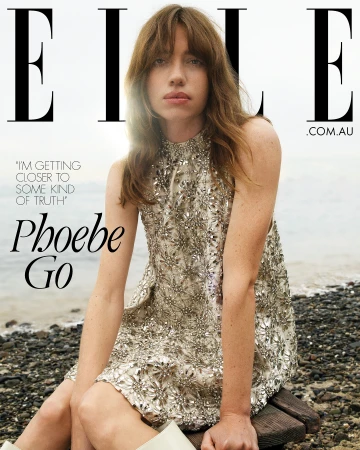 Woman in an embellished silver dress seated on a wooden pier by the water with magazine cover text overlay