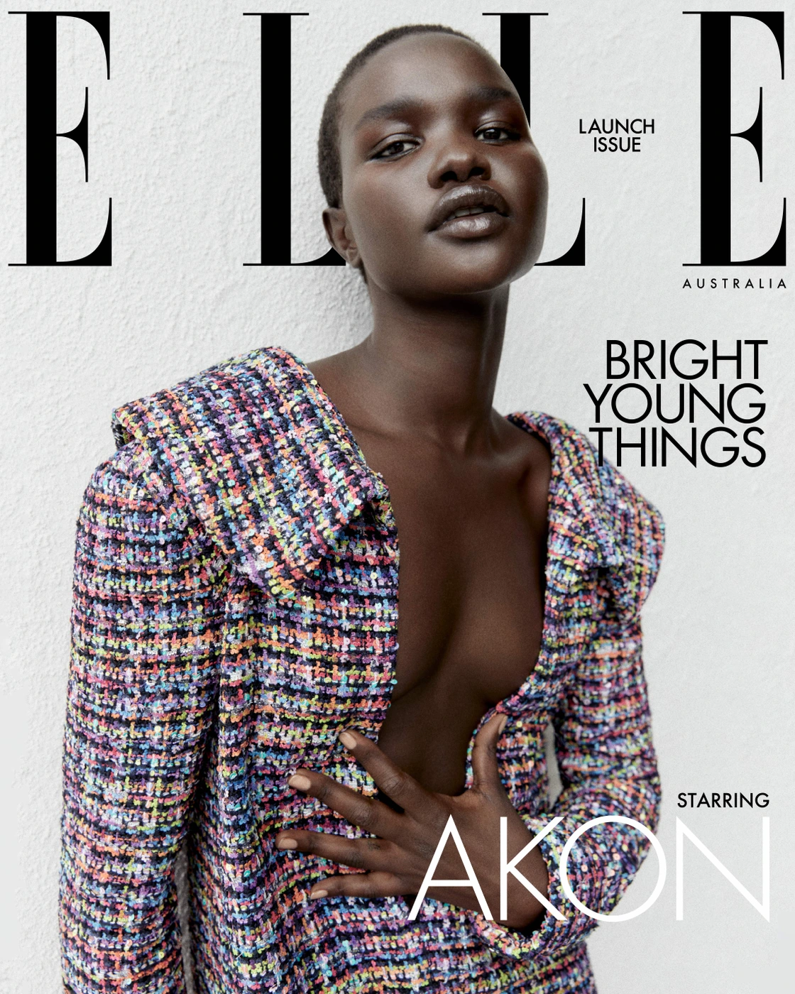 Close-up portrait of a Black female model wearing a textured multi-color tweed blazer against a textured white wall.