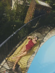 Woman in red one-piece swimsuit lounging on a yellow towel by a pool, shot from an elevated angle by Eminente Creative Production