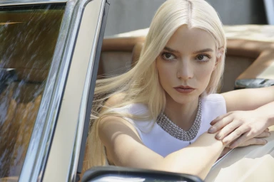 Anya Taylor-Joy with long blonde hair wearing a white top and pearl necklace, seated in a classic car.