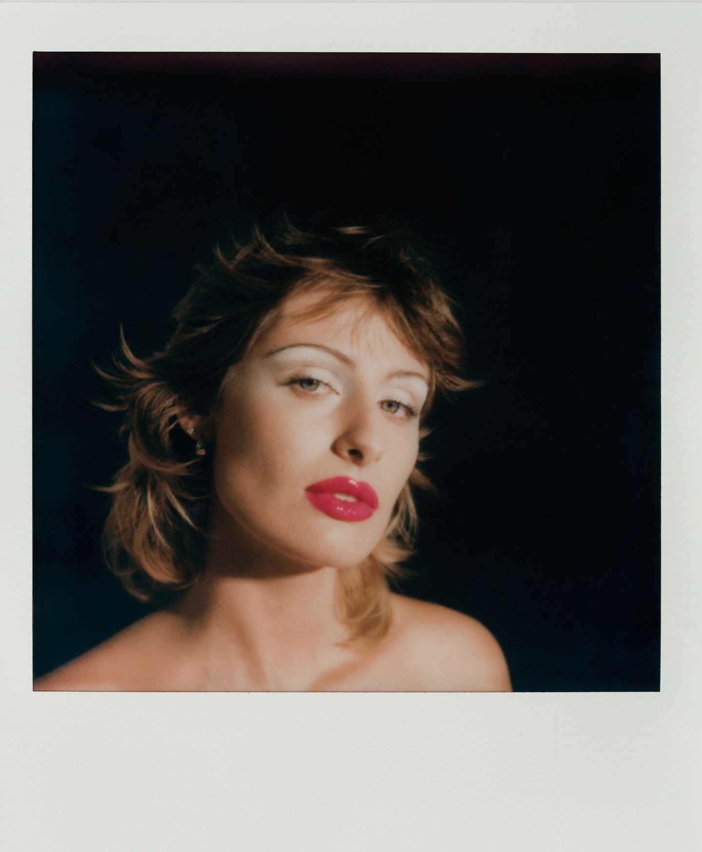 Headshot of a model with dramatic white eyeshadow and bright pink lips against a dark background in a studio setting.