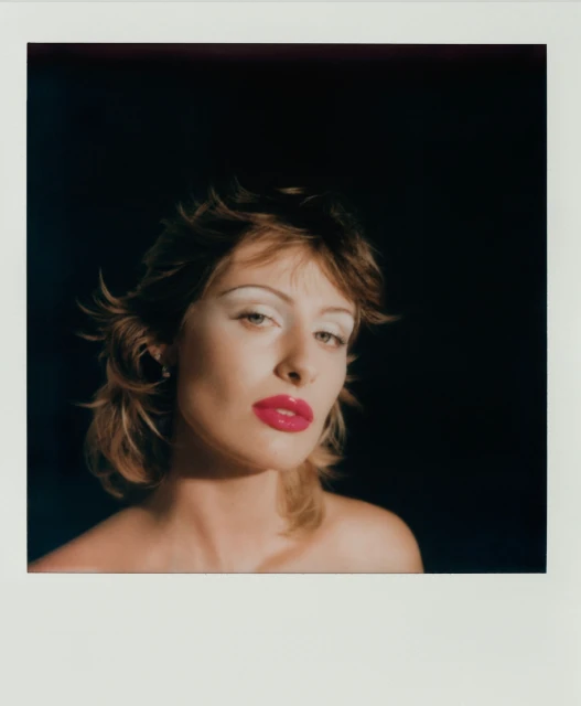 Headshot of a model with dramatic white eyeshadow and bright pink lips against a dark background in a studio setting.