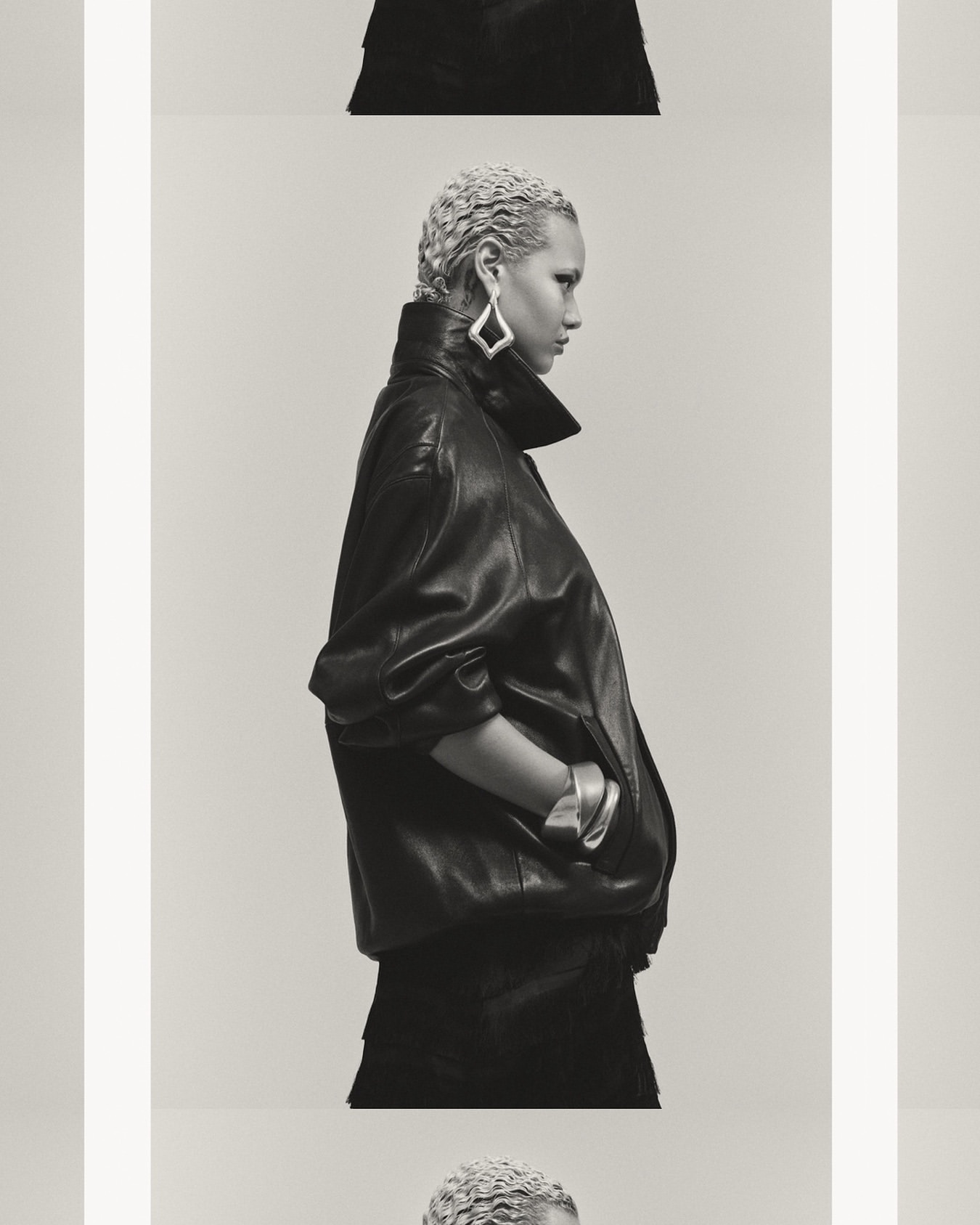 Profile shot of an adult female model with bleached blonde hair wearing a black leather jacket, silver bracelet, and diamond earrings in a photo studio.