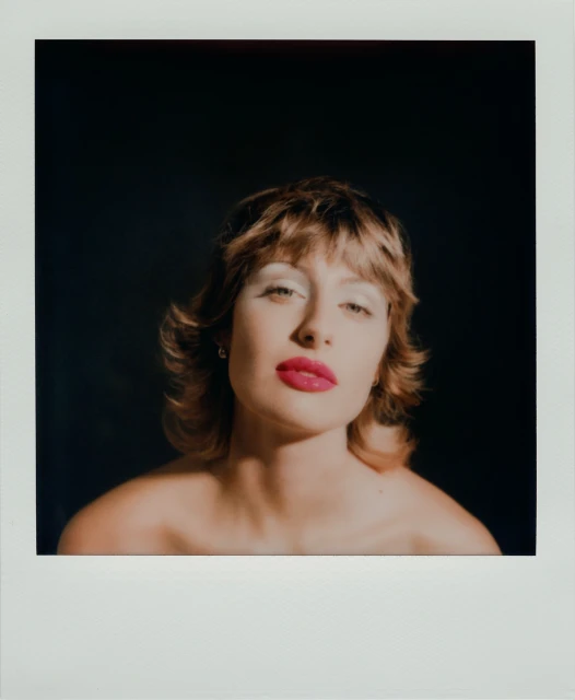 Glamour headshot of a light-skinned woman with short brown hair, red lipstick, and dramatic white eyeshadow against a dark backdrop.