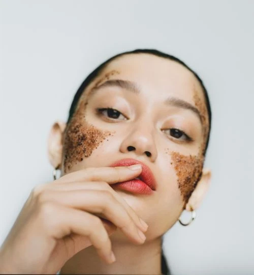 Close-up portrait of a young woman with dark hair and a light complexion, posing with skincare product on her face in a beauty shot.