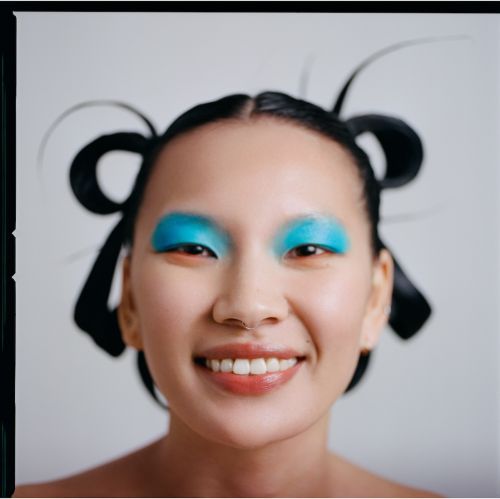 Close-up of an Asian woman with a wide smile, bright blue eyeshadow, and an elaborate hairstyle with black ribbons.