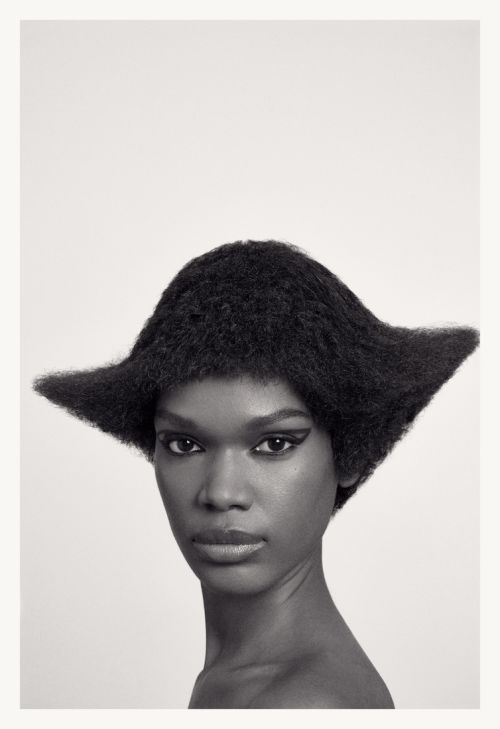 Close-up portrait of an African American woman with striking black winged eyeliner and an avant-garde hair design against a white backdrop.