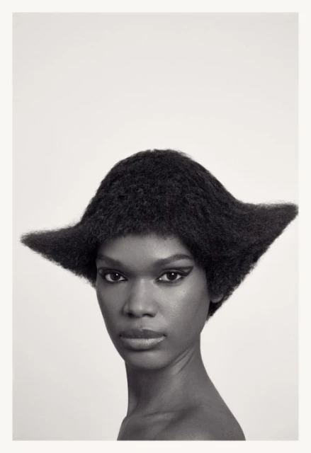 Close-up portrait of an African American woman with striking black winged eyeliner and an avant-garde hair design against a white backdrop.