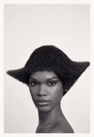 Close-up portrait of an African American woman with striking black winged eyeliner and an avant-garde hair design against a white backdrop.