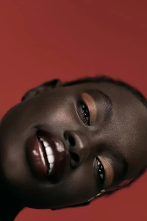 Close-up portrait of a Black woman with glossy dark lips against a solid dark red background captured by Saloni Agarwal.
