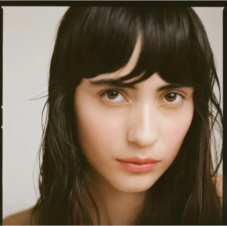 Close up portrait of a woman with dark hair and bangs against a neutral background photographed by Saloni Agarwal