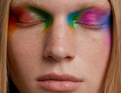 Extreme close-up of a person with colourful blended eyeshadow covering their closed eyes, fair skin, and light blonde hair.