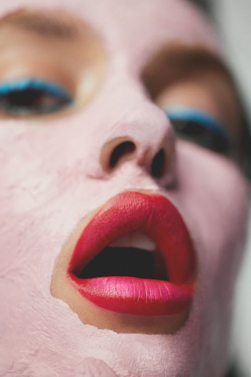 Close-up portrait of a person's face with pink face makeup and bright pink lipstick and blue eyeliner, showcasing beauty and makeup.