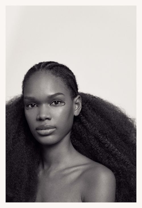 Portrait of an African-American woman with natural hair styled in pigtails, wearing graphic eyeliner, and posing against a white background.