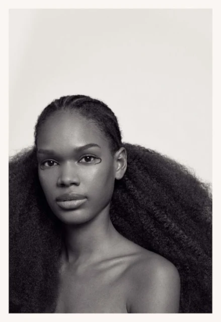 Portrait of an African-American woman with natural hair styled in pigtails, wearing graphic eyeliner, and posing against a white background.