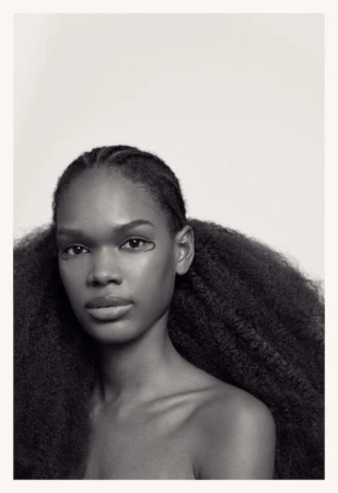 Portrait of an African-American woman with natural hair styled in pigtails, wearing graphic eyeliner, and posing against a white background.