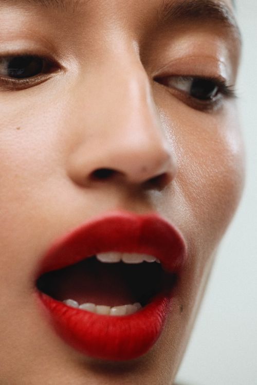 Close-up portrait of a model with vibrant red lipstick and parted lips against a neutral background by Saloni Agarwal