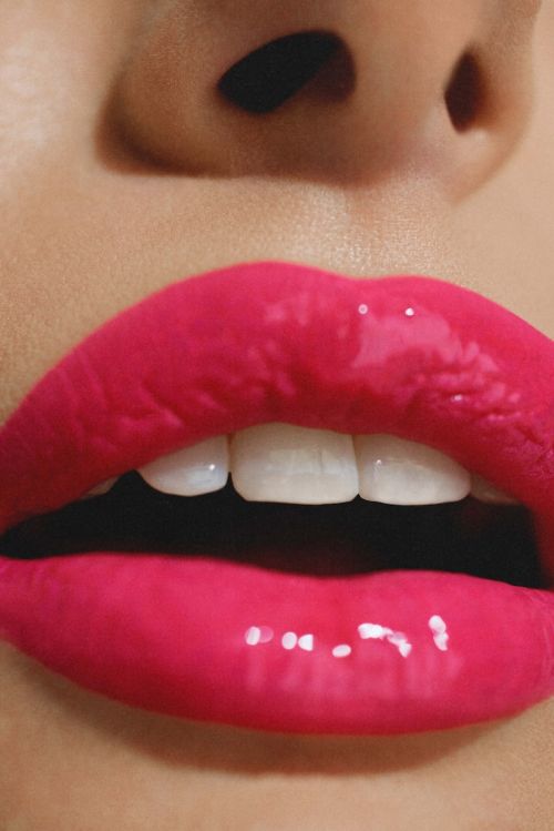 Close-up on a woman's face with glossy pink lips, showcasing white teeth, fair skin tone, and natural makeup.