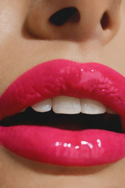 Close-up on a woman's face with glossy pink lips, showcasing white teeth, fair skin tone, and natural makeup.