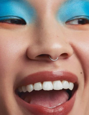 Close up portrait of smiling person with bright blue eyeshadow and a silver septum ring