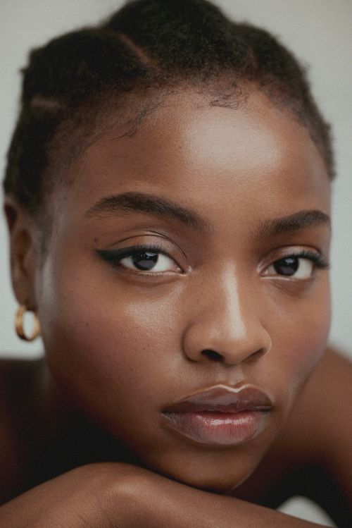 Close-up portrait of an African American woman with an introspective expression, dark hair, and gold hoop earring against a white background.