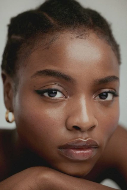 Close-up portrait of an African American woman with an introspective expression, dark hair, and gold hoop earring against a white background.