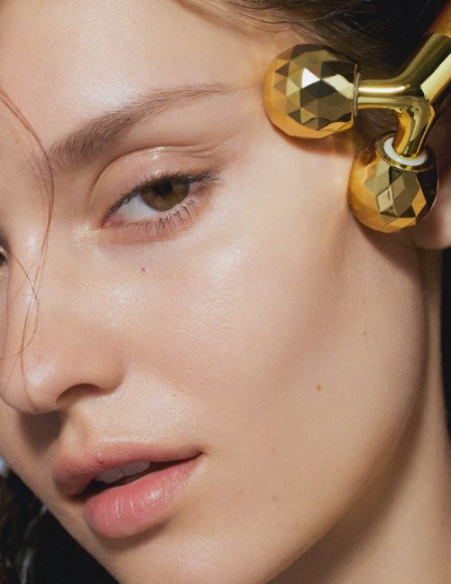 Close-up of a fair-skinned woman's face as she receives a facial massage with a gold metal roller, highlighting skincare and beauty.