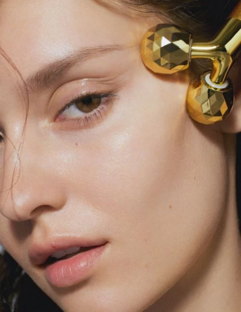 Close-up of a fair-skinned woman's face as she receives a facial massage with a gold metal roller, highlighting skincare and beauty.
