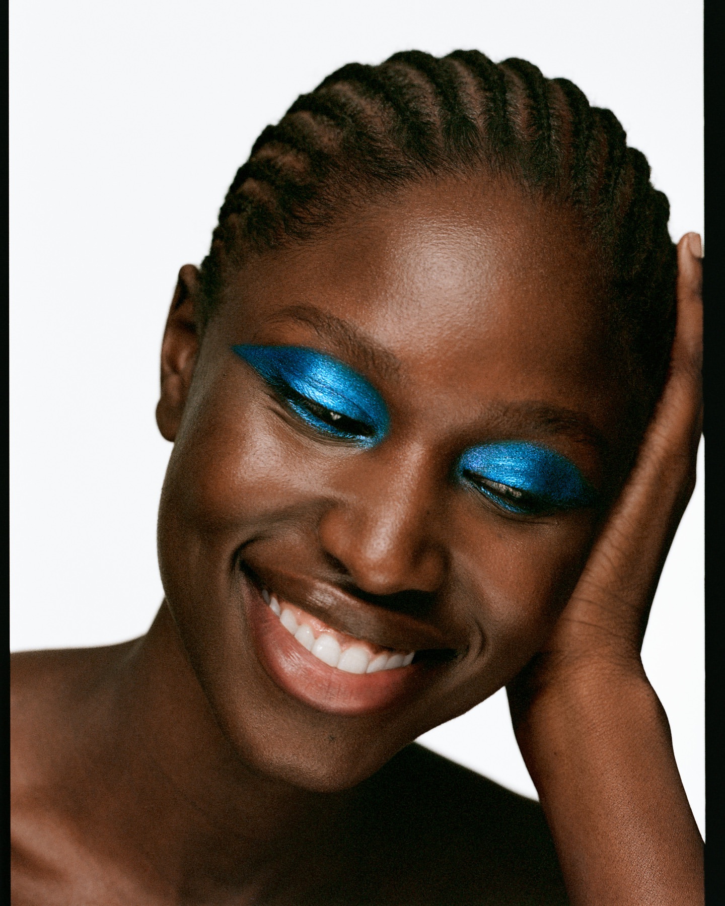 Close-up beauty portrait of smiling African-American adult female with blue eyeshadow makeup and braided hair against a white background.
