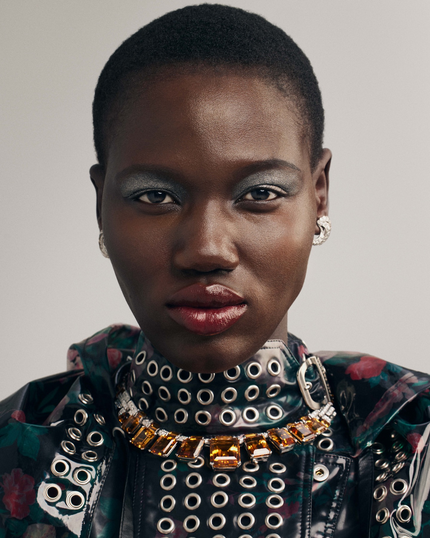 Close-up studio shot of a Black woman with short hair wearing a statement necklace and a floral jacket with grommets. Fashion and beauty.