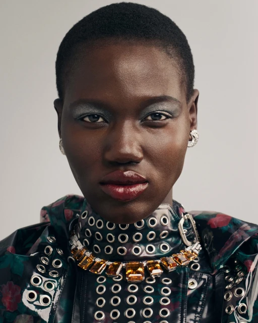 Close-up studio shot of a Black woman with short hair wearing a statement necklace and a floral jacket with grommets. Fashion and beauty.