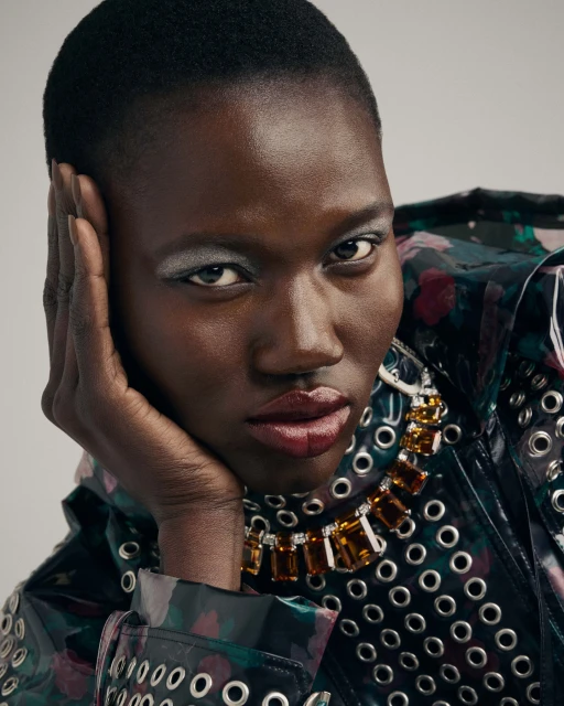 Portrait of a short-haired African American female model with silver eyeshadow and a jewel-toned necklace, posing in a patterned jacket.