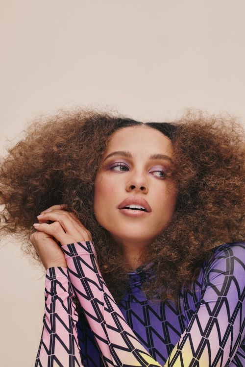 Portrait of a beautiful adult female model with curly hair, wearing patterned top. Eye-level shot in a photo studio with soft lighting.