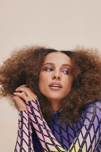 Portrait of a beautiful adult female model with curly hair, wearing patterned top. Eye-level shot in a photo studio with soft lighting.