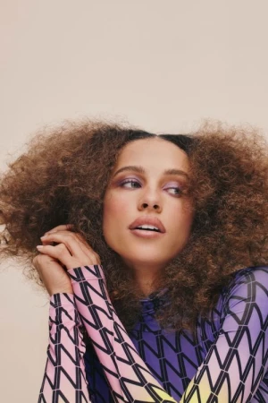 Portrait of a beautiful adult female model with curly hair, wearing patterned top. Eye-level shot in a photo studio with soft lighting.