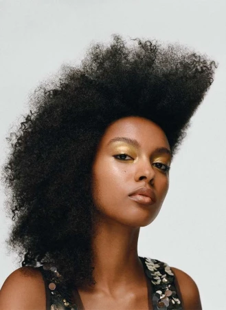 Close up portrait of a Black woman with voluminous textured afro hair wearing metallic gold eyeshadow against a plain white background
