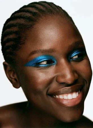 Close-up portrait of a Black woman smiling with bright metallic blue eyeshadow against a white backdrop