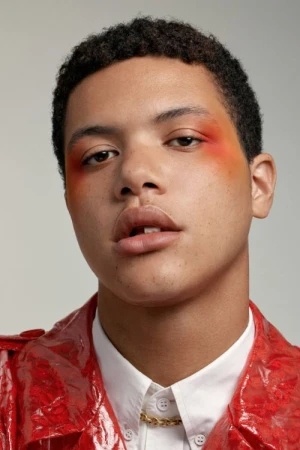 Portrait of a man wearing a red coat and white collared shirt with orange makeup around his eyes