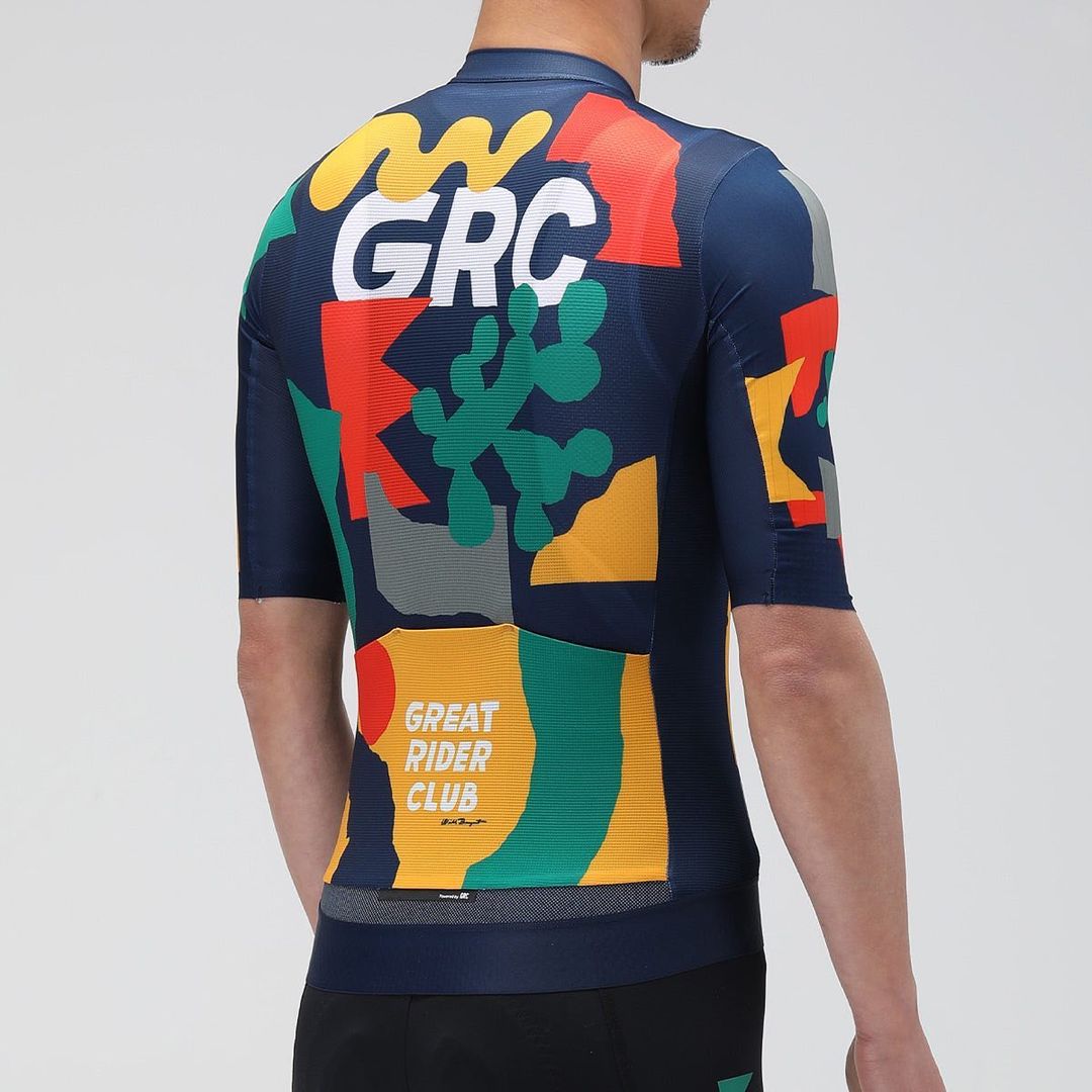 Back view of a person in a patterned cycling jersey with graphic elements, GRC text, and geometric shapes against a neutral backdrop.