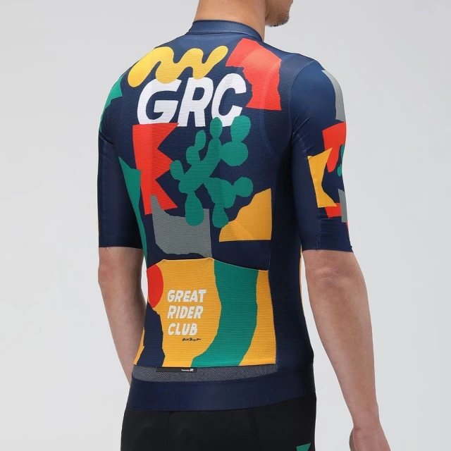 Back view of a person in a patterned cycling jersey with graphic elements, GRC text, and geometric shapes against a neutral backdrop.