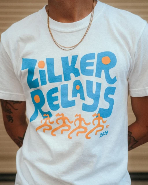 Person wearing a white t-shirt with the words 'Zilker Relays' and four figures printed on the front along with a gold chain necklace.