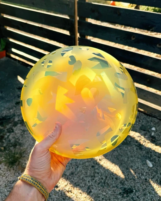 Hand holding an iridescent yellow frisbee outdoors against a fence, showcasing its texture and color in a natural setting.