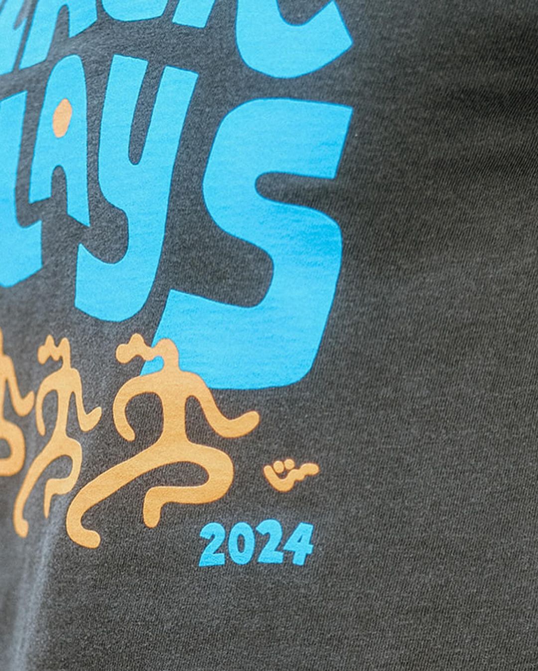 Close-up of a gray t-shirt with a turquoise graphic, tan stick figures, and the year 2024 printed on it.