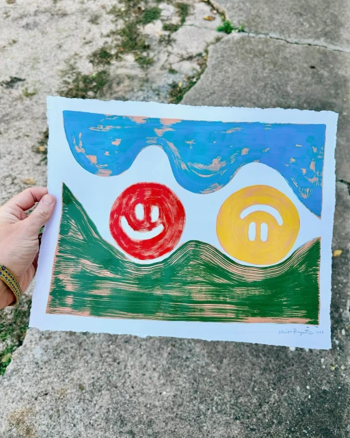 Printmaking artwork featuring two stylized smiley faces in red and yellow, set against a textured blue sky and green hills.