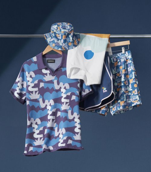 Display of a patterned polo shirt, shorts and bucket hat hanging on a metal clothing rack against a dark blue background.
