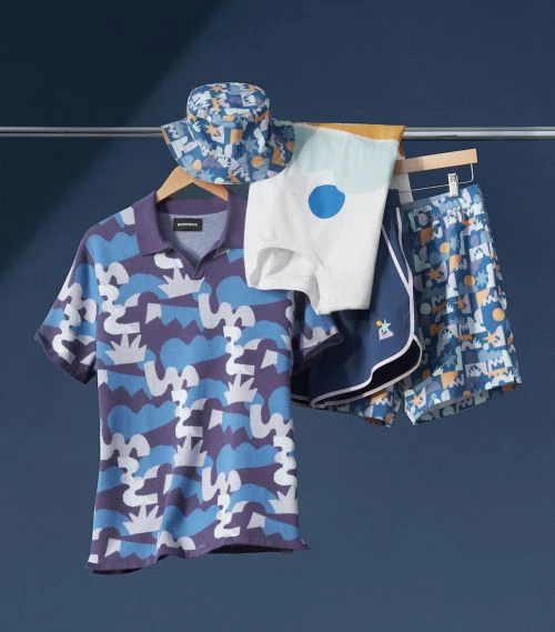 Display of a patterned polo shirt, shorts and bucket hat hanging on a metal clothing rack against a dark blue background.