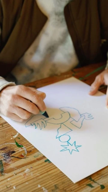 Close-up of a person drawing a blue line art illustration of a figure and a star on white paper using a blue marker pen.