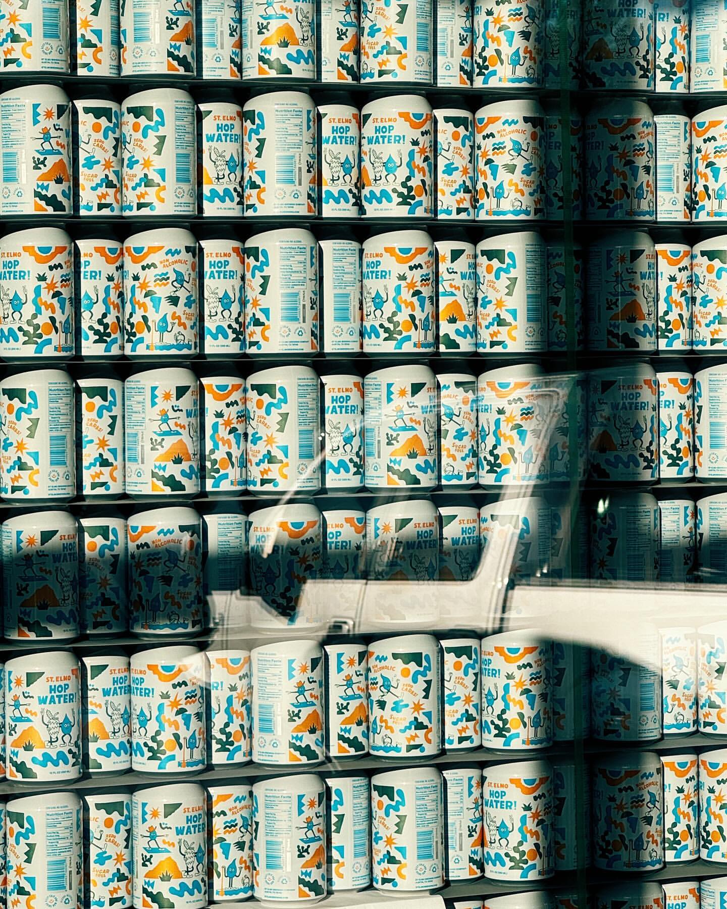 Shelves stacked with cans of flavored sparkling water featuring colorful abstract graphics on white cans in a retail setting.